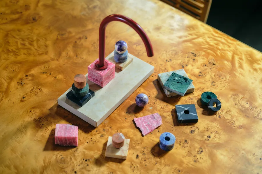 Dornbracht Atelier tap by Fabian Freytag with red curved spout, rhodochrosite cube and stacked stone handles on a burl wood table